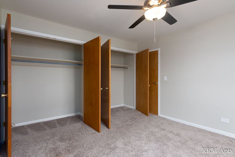 Carpeted bedroom with ceiling fan and double closet with wood doors, Park Avenue apartment 204